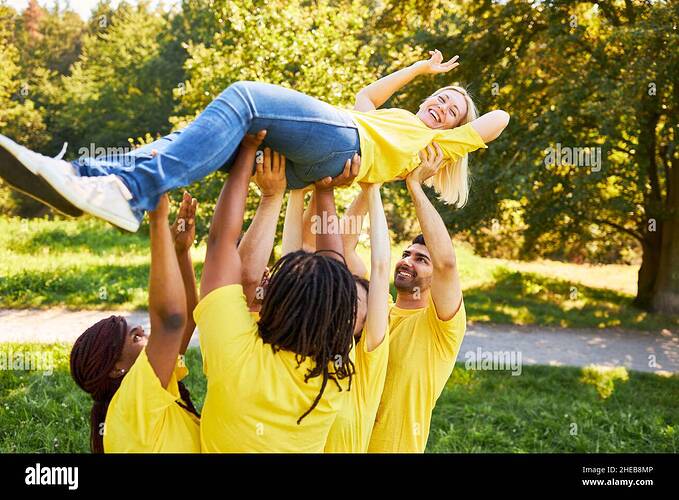 laughing-woman-is-lifted-up-by-young-people-in-team-building-workshop-in-summer-2HEB8MP