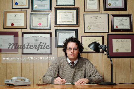 700-00284691em-man-at-desk-in-front-of-diplomas-stock-photo